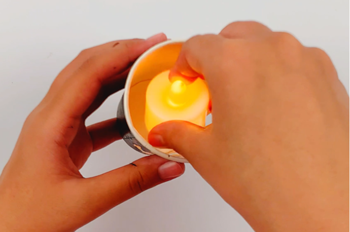 Two hands placing a battery powered candle light inside the paper cup.