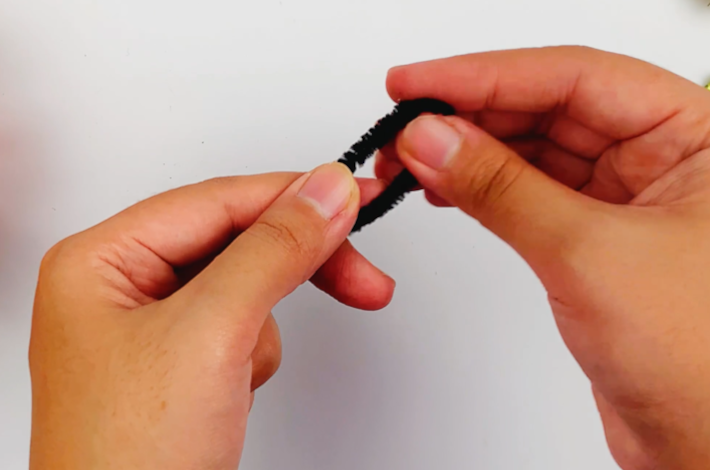 Two hands bending a small section of the pipe cleaner in half.