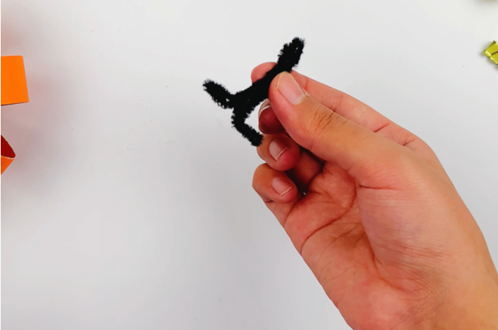 A hand holding the twisted craft pipe cleaner with the two ends bent out at a 90 degree angle.