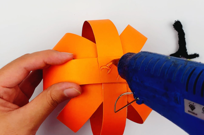 A glue gun applying glue to the top of the pumpkin.