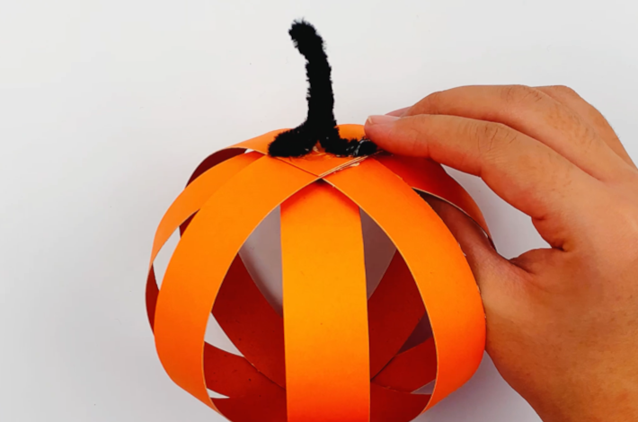 Two hands securing the stalk to the top of the pumpkin.