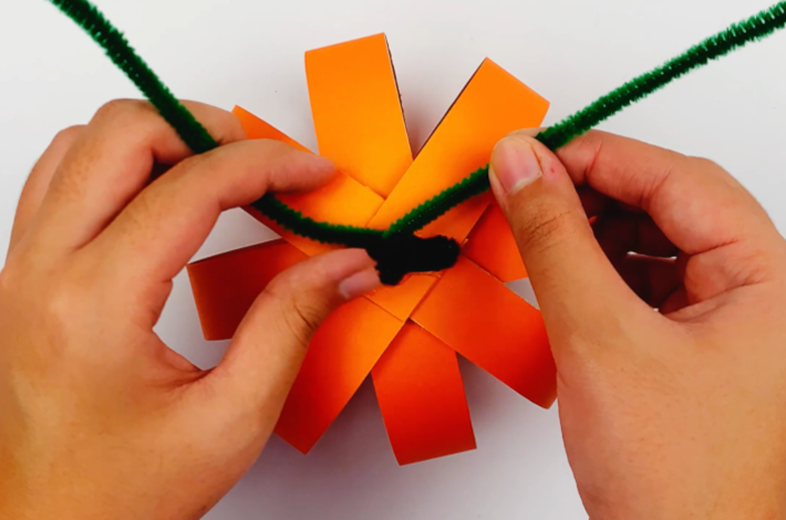 Two hands securing another craft pipe cleaner around the stalk.