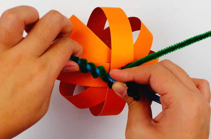Two hands using a pencil to twirl the craft pipe cleaner sections extending from the stalk.
