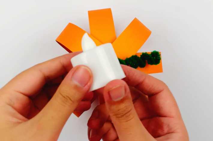 Two hands holding a battery powered light, ready to be put inside the pumpkin.