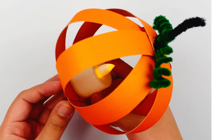 Two hands holding the finished pumpkin with the light inside.