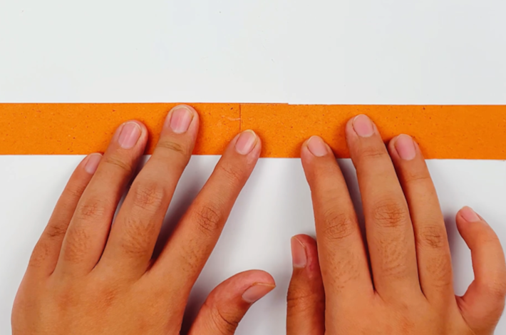 Two hands sticking two strips together.