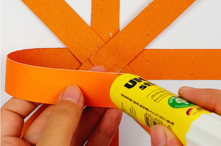 Two hands adding glue to the far end of one of the strips.