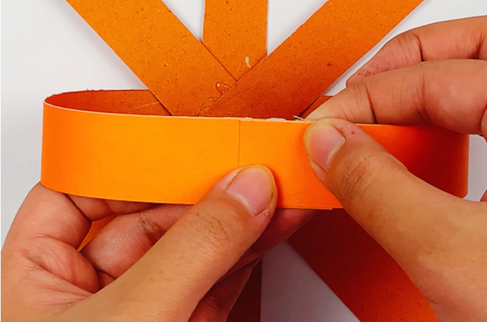 Two hands glueing the strips together at the top of the pumpkin.