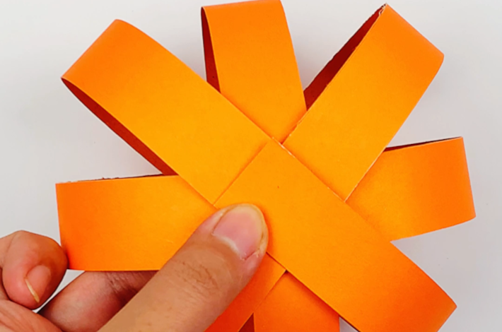 Two hands holding all the glued strips in place on the top of the pumpkin.