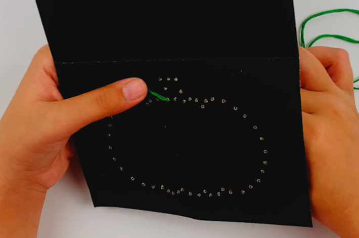 Two hands holding the end of the green string with a thumb securing it.