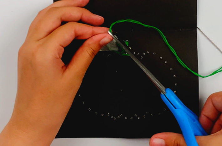 Two hands cutting the end of the green thread.