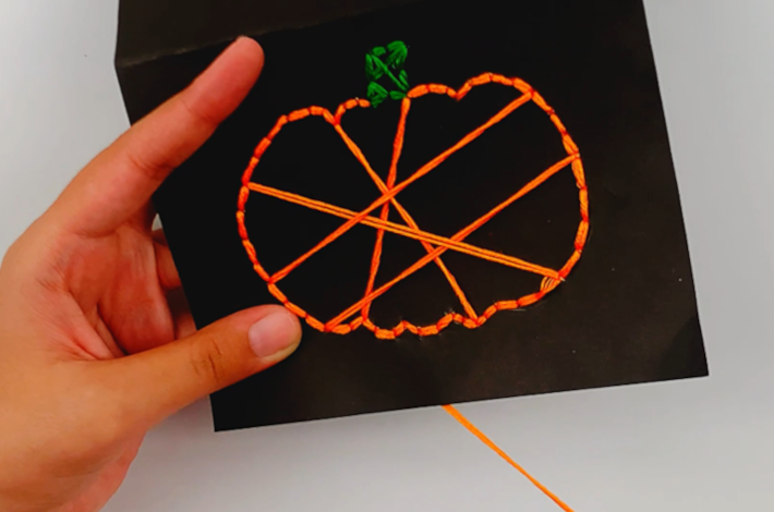 Two hands criss-corssing the thread along the inner section of the pumpkin. 
