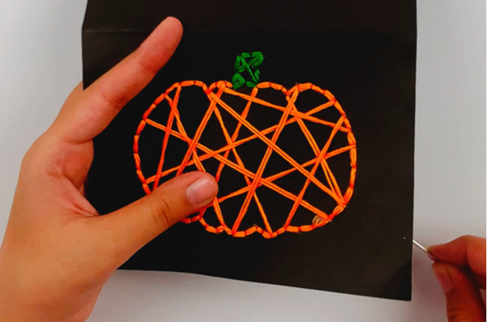 Two hands showing the pumpking with orange thread criss-crossing it all over. 
