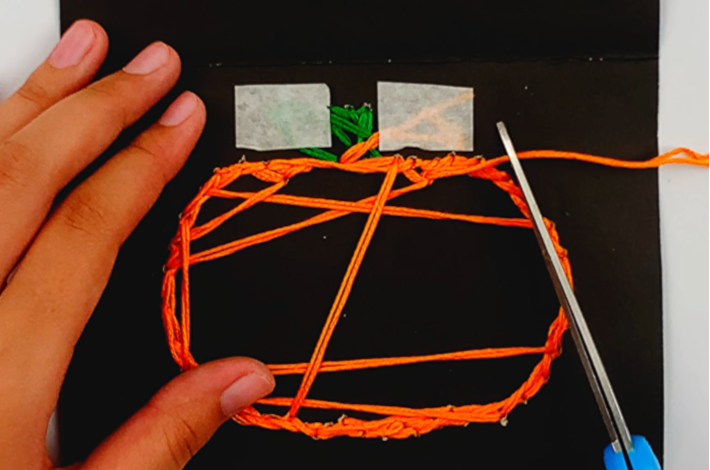 Two hands cutting the thread and securing it to the back of the poster card under the painter's tape used earlier. 