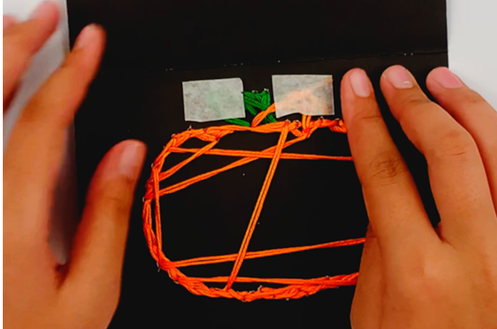 Two hands securing the thread under the painter's tape. 