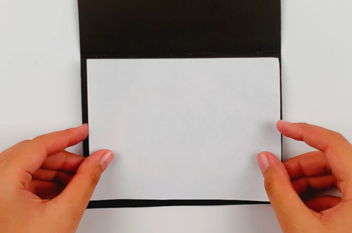 Two hands glueing the bottom section of the A4 page to the poster board.