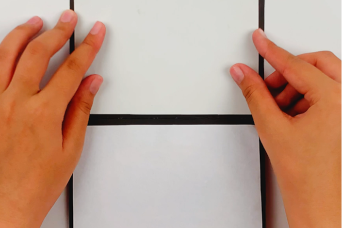 Two hands glueing the top section of the A4 page to the poster board.