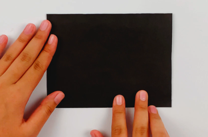 Two hands flipping the A4 poster card sideways so it can be opened from top to bottom. 