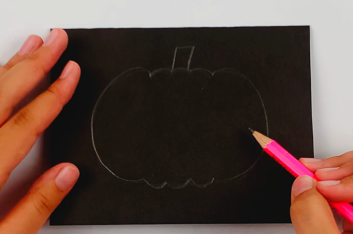 Pencil drawing the shape of a pumpkin on the poster board. 