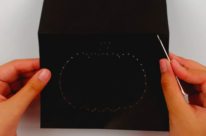 Two hands holding the needle and showing the spacing between all the holes poked in it. 