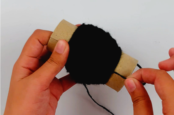 Two hands holding the cardboard roll with a lot of wool wrapped around it.