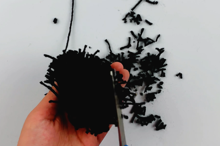 Two hands trimming the edges of the wool to form a popm pom.