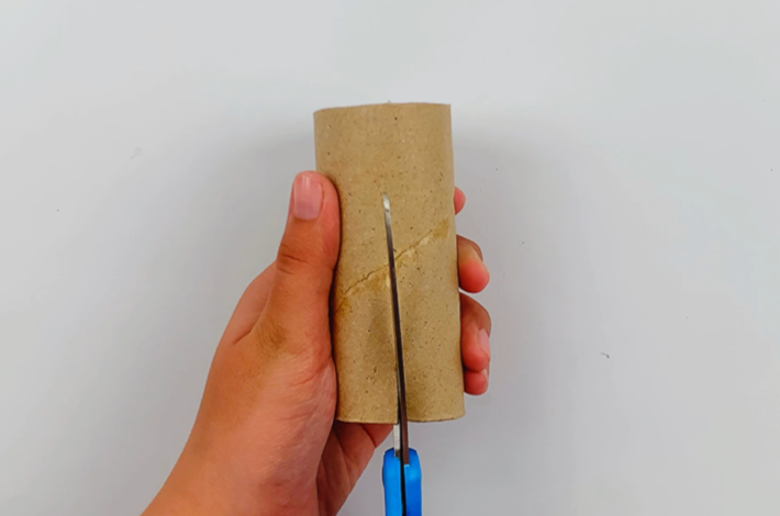 Two hands cutting a short slit at the bottom of the inner cardboard tube from a toilet roll.