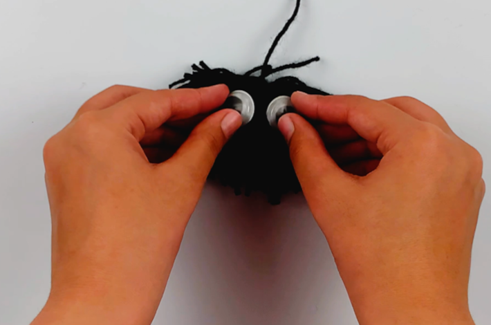 Two hands placing googly eyes on the pom pom.