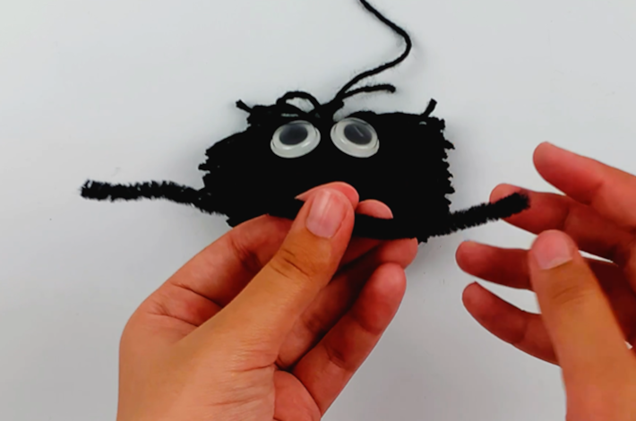 Two hands holding a craft pipe cleaner that will form the spider's legs.