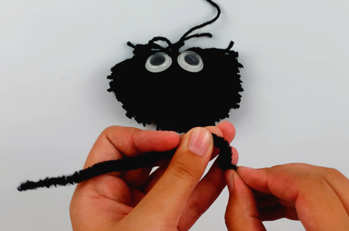 Two hands bending the first craft pipe cleaner to form the spider's leg.