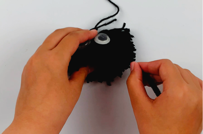 Two hands pushing the first spider leg into the pom pom to secure it.