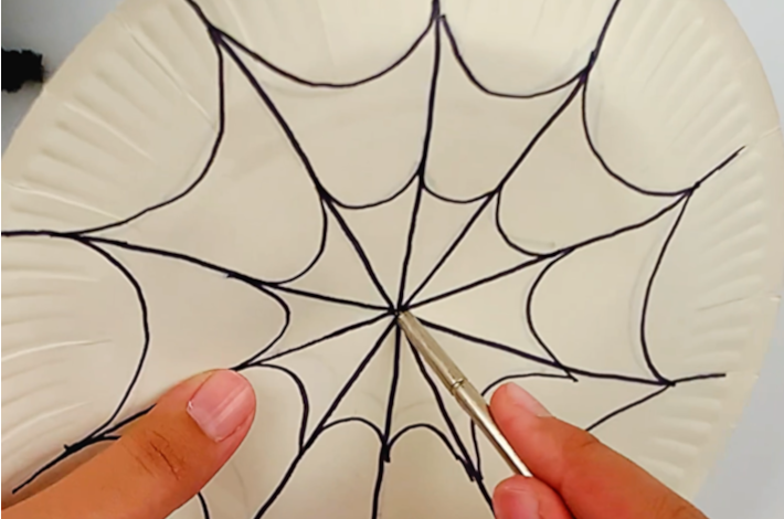 Two hands punching a hole in the center of the paper plate.