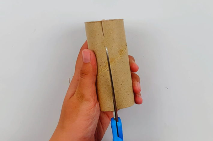 Two hands cutting a short slit at the bottom of the inner cardboard tube from a toilet roll.