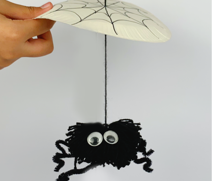 Two hands playing with the pom pom spider.