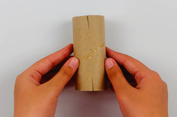 Two hands cutting holding the inner cardboard tube from a toilet roll showing the two slits that have been cut.