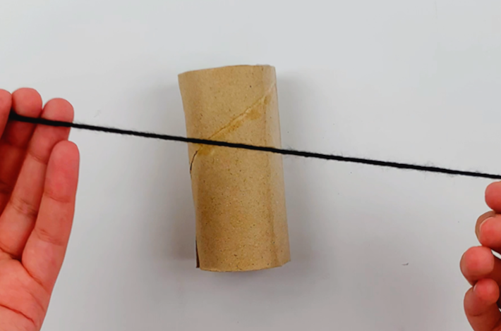 Two hands holding a length of black wall over the cardboard tube.