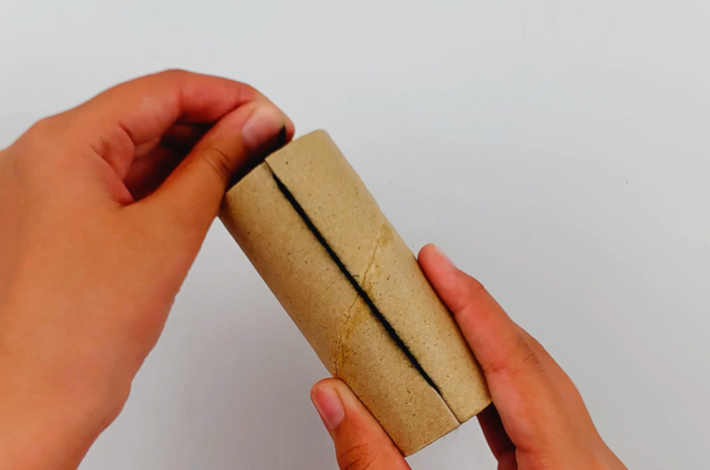 Two hands pulling the ends of the wool down through the tube to secure them while the length of the wool runs along the tube.
