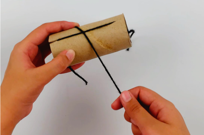 Two hands wrapping a ball of wool around the cardboard roll which has been turned 90 degrees.