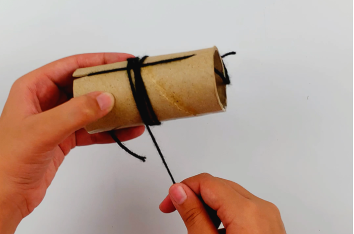 Two hands wrapping more wool around the cardboard roll.