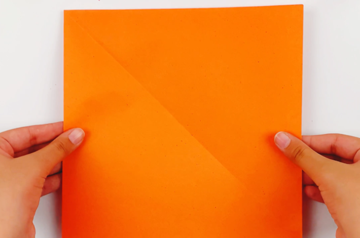 Two hands holding a square piece of orange paper. 