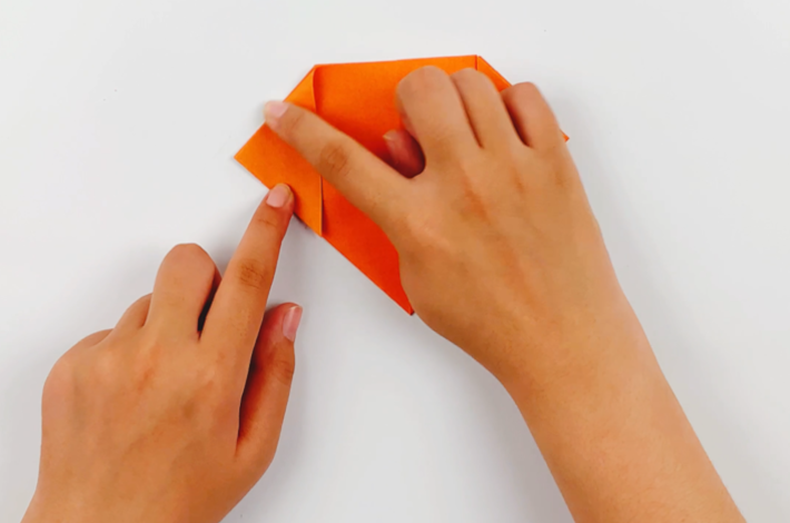 Two hands making the same fold on the left-hand side after the paper has been flipped over. 