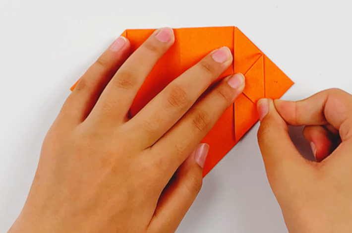Two hands folding the top section of the triangle on the right-hand side inwards. 
