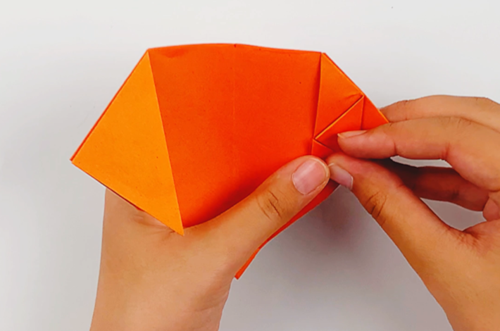 Two hands folding the bottom triangle on the right side of the paper upwards, towards the fold made before. 