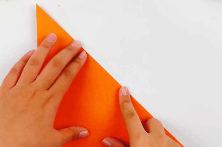 Two hands folding the paper in half at a 45-degree angle to form a triangle. 