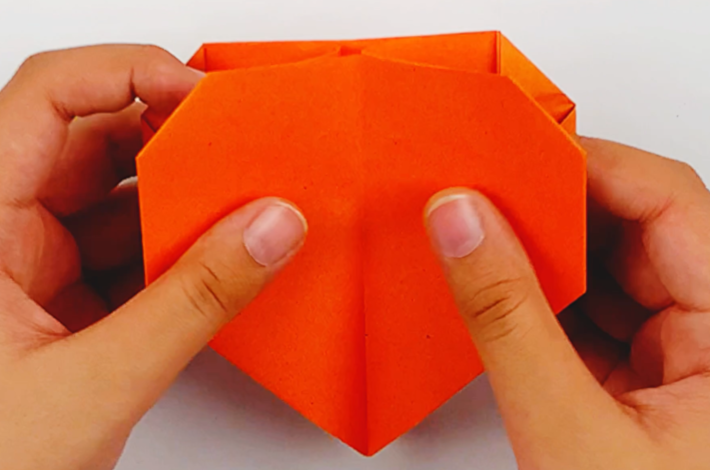 Two hands folding the sides of the paper with the folds previously made inwards. 