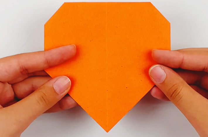 Two hands holding the paper after the folds have been tucked inwards. 