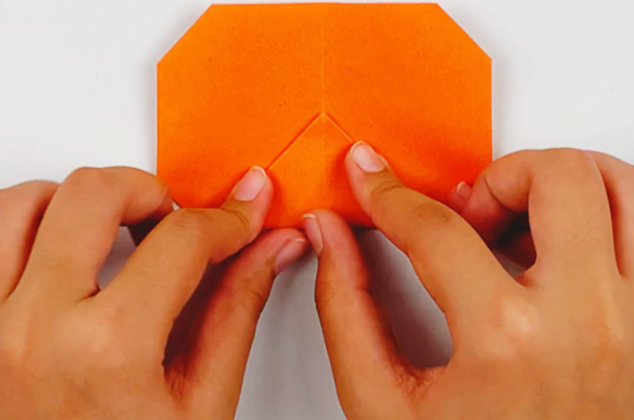Two hands folding the triangle at the bottom of the paper upwards. 