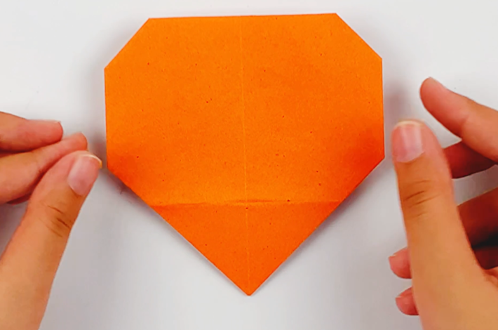 Two hands folding the triangle at the bottom of the paper underneath as well before returning it to the original position. 
