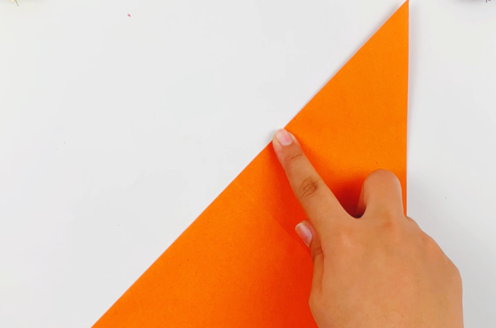 Two hands folding the paper at a 45-degree angle from top left to bottom right. 