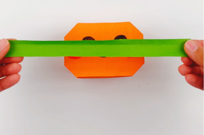 Thow hands holding a long strip of green paper. 